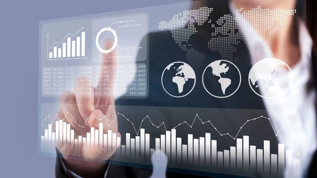 Mão de uma pessoa tocando uma interface digital transparente com gráficos, mapas globais e dados estatísticos futurísticos em exibição.