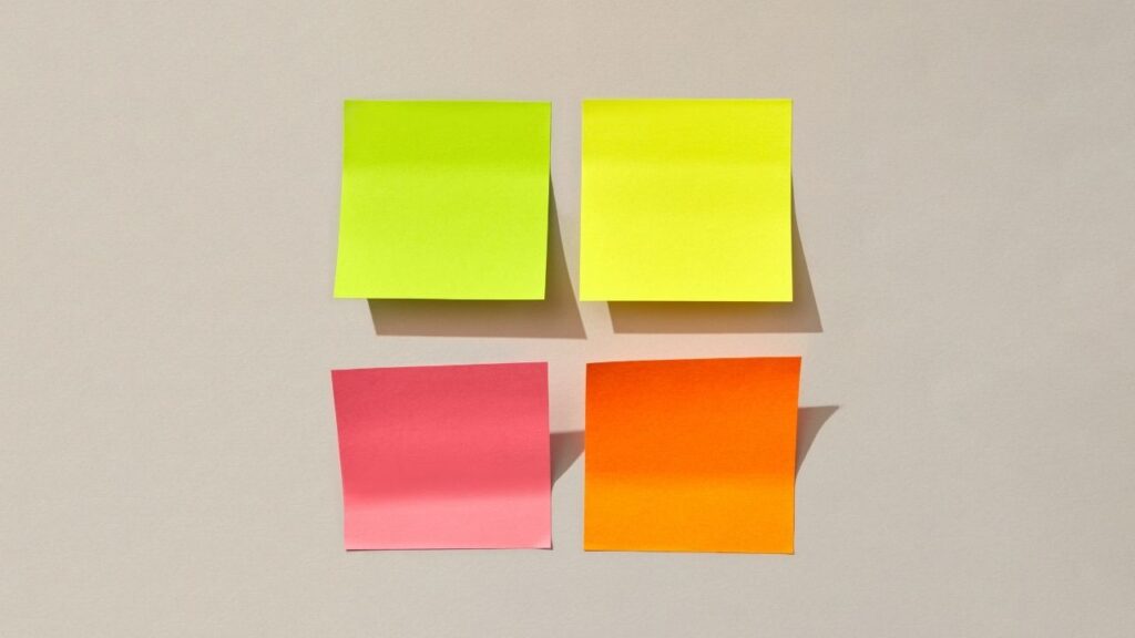 Plano focado em quatro post-its organizados em tons de verde, amarelo, rosa e laranja em uma superfície, representando um planejamento visual.