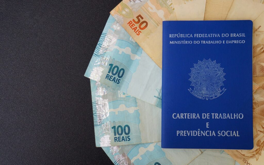 carteira de trabalho em cima de notas de cinquenta e cem reais fazendo referência aos valores de cálculo judicial trabalhista