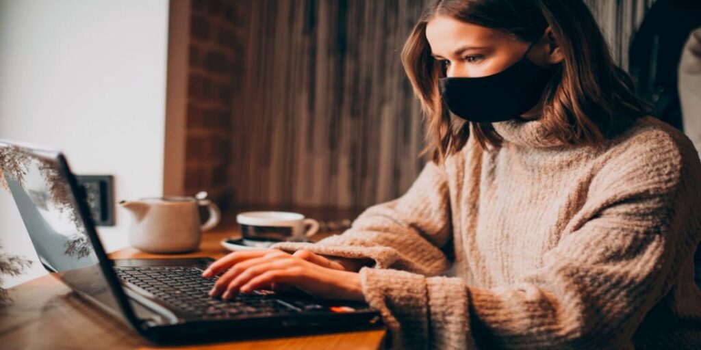 Imagem de mulher trabalhando em notebook, de máscara