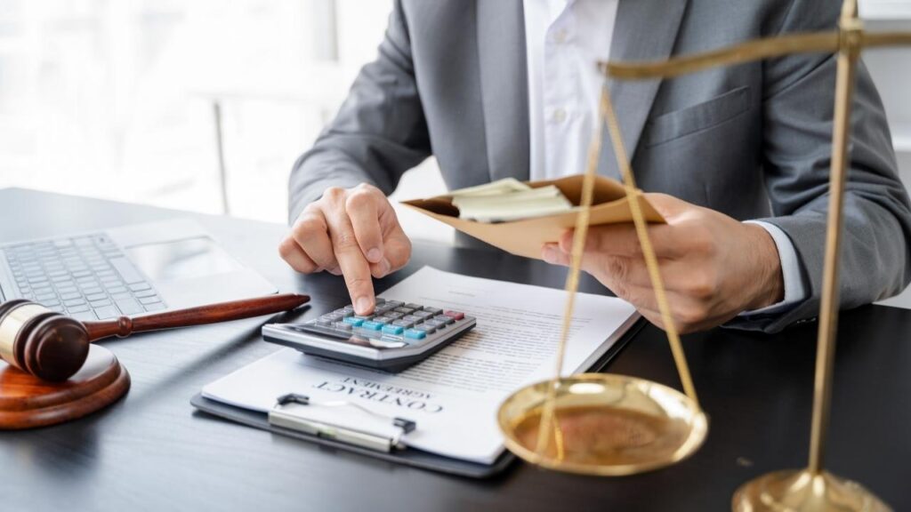 Homem calculando valores com dinheiro em mãos e balança da justiça, simbolizando contabilidade e direito financeiro.