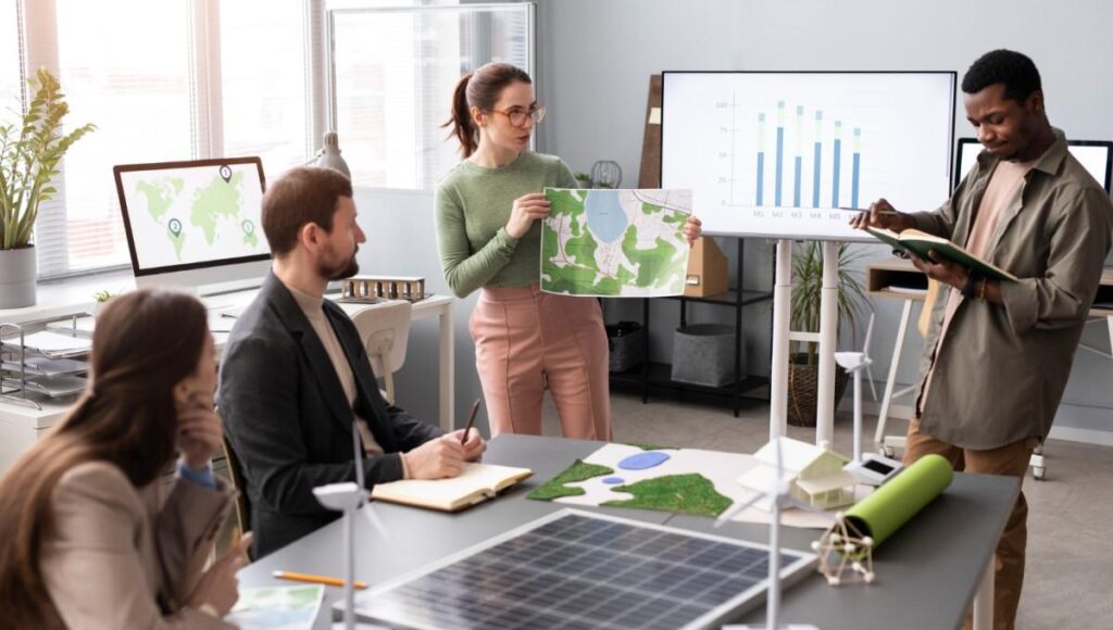 Equipe de profissionais em reunião discutindo estratégias de sustentabilidade, com gráficos e mapas de energia renovável sobre a mesa e em telas ao fundo, simbolizando planejamento de práticas empresariais sustentáveis.