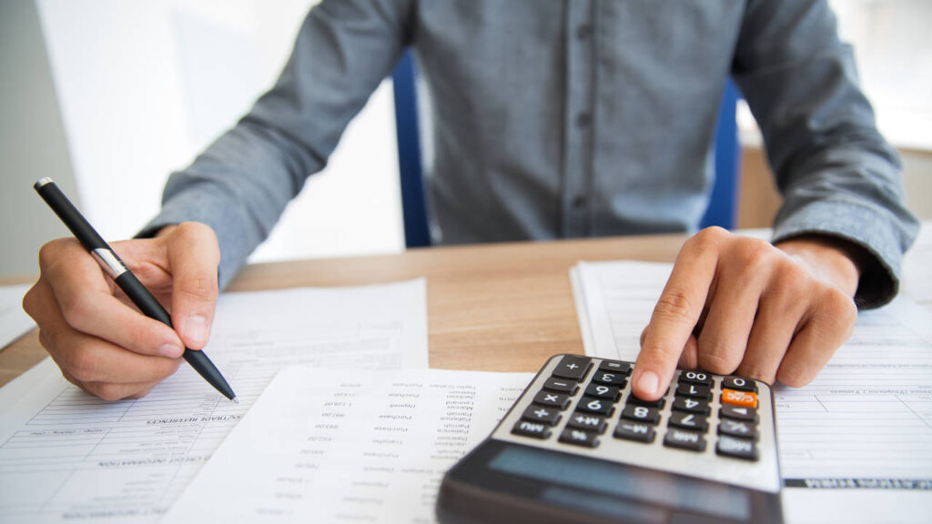 Pessoa analisando documentos financeiros enquanto utiliza uma calculadora.