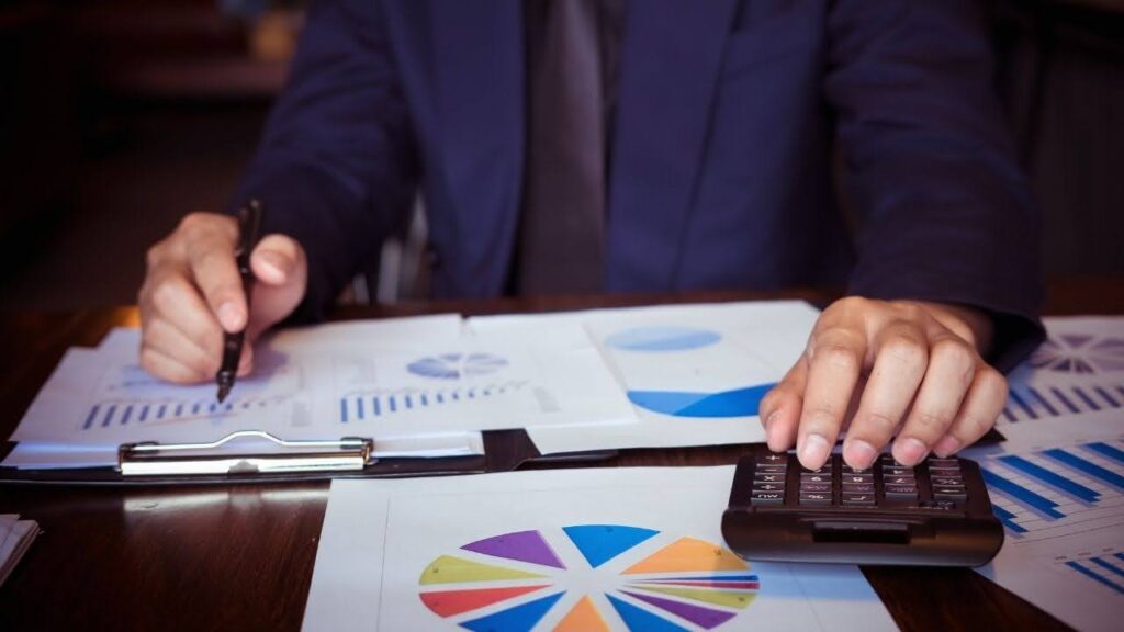 Homem de negócios analisando relatórios financeiros com gráficos e calculadora em uma mesa de trabalho.