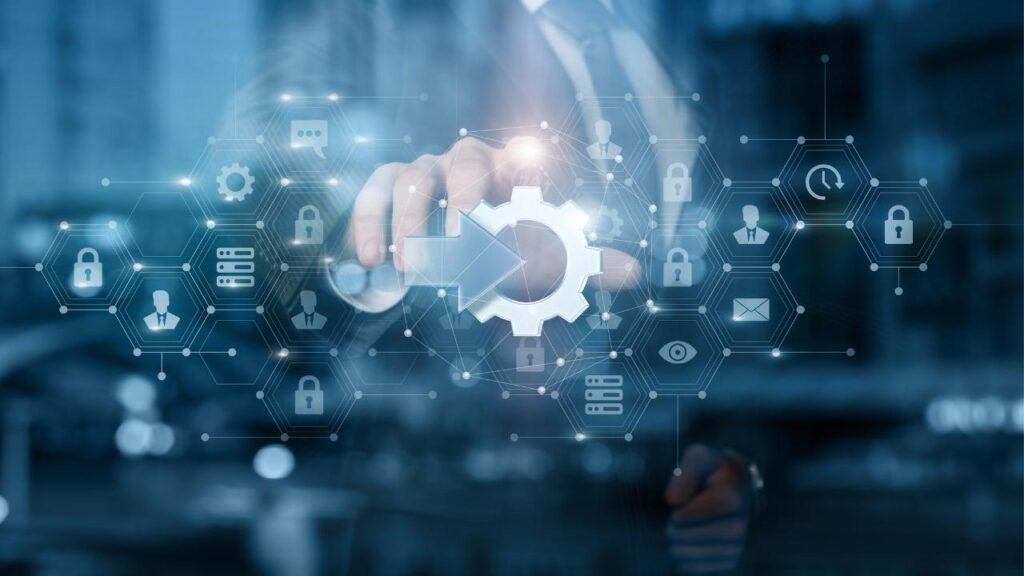 Uma mão tocando um ícone digital em forma de engrenagem. Há elementos gráficos ao redor, como cadeados e conexões, simbolizando segurança digital e processos interconectados.