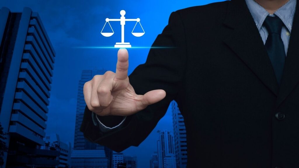 Homem de terno apontando para um ícone digital de balança da justiça sobre um fundo azul.