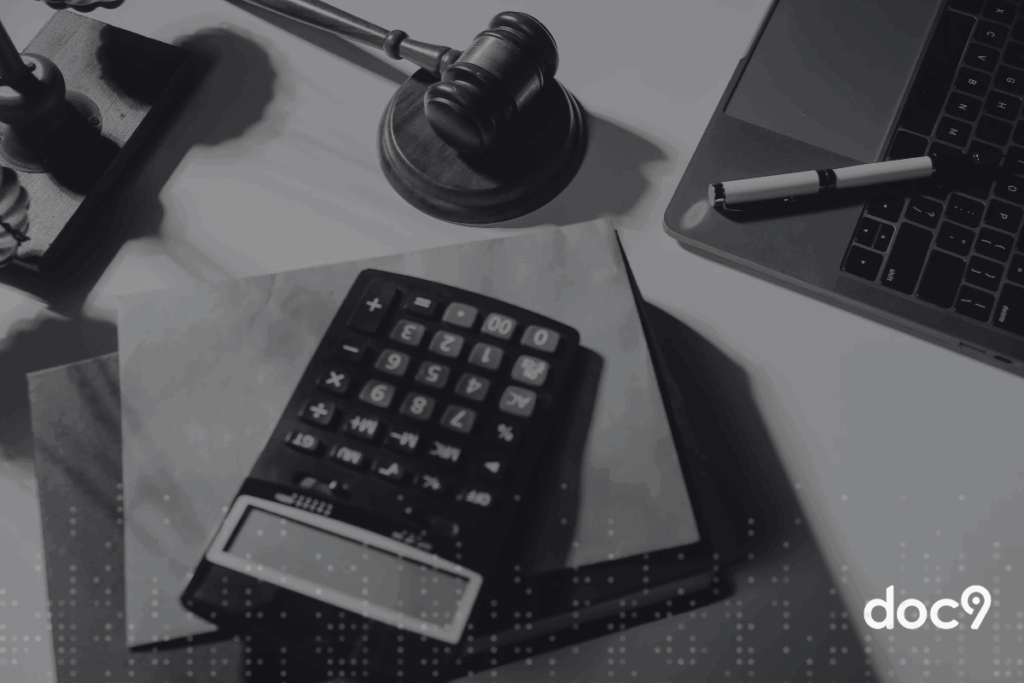Imagem de uma mesa de escritório com uma calculadora, laptop, gavel de juiz, caneta e papel, representando temas de direito, advocacia e matemática.